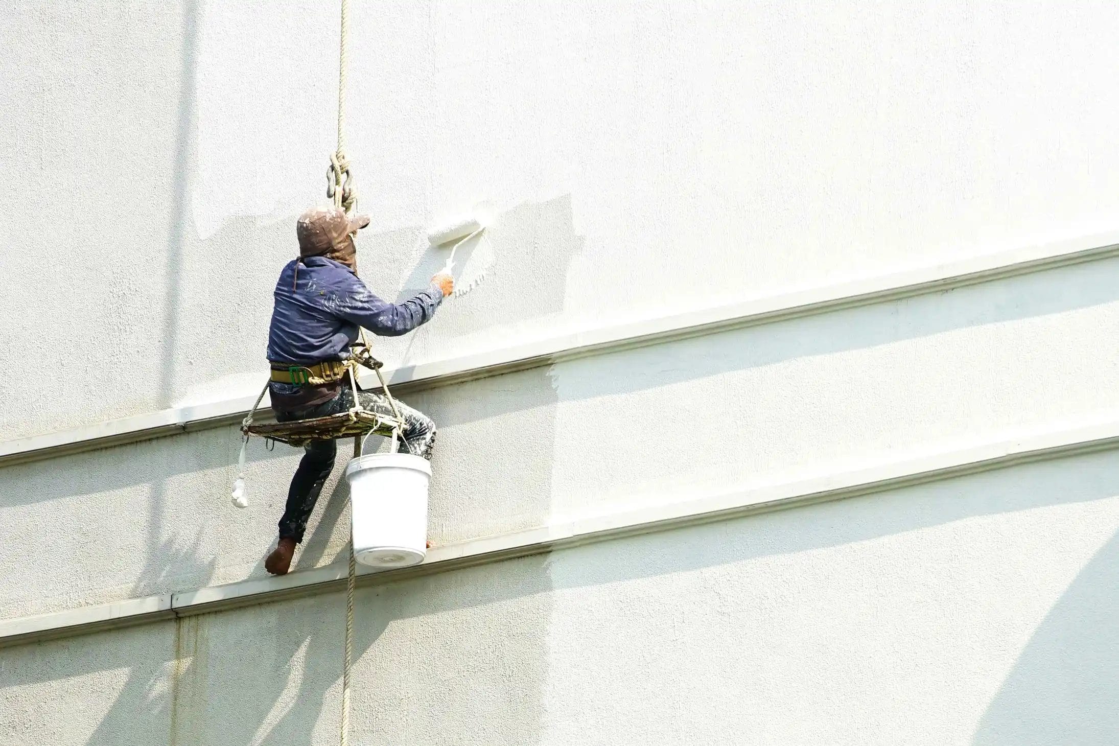painter-hanging-white-building servicio de hidrolavado de grandes estructuras